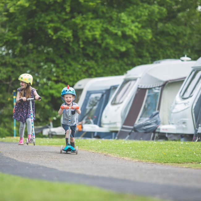 children playing on scooter by caravans at Forest Glade