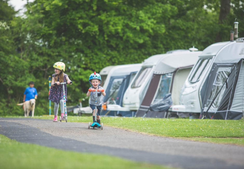 children playing on scooter by caravans at Forest Glade