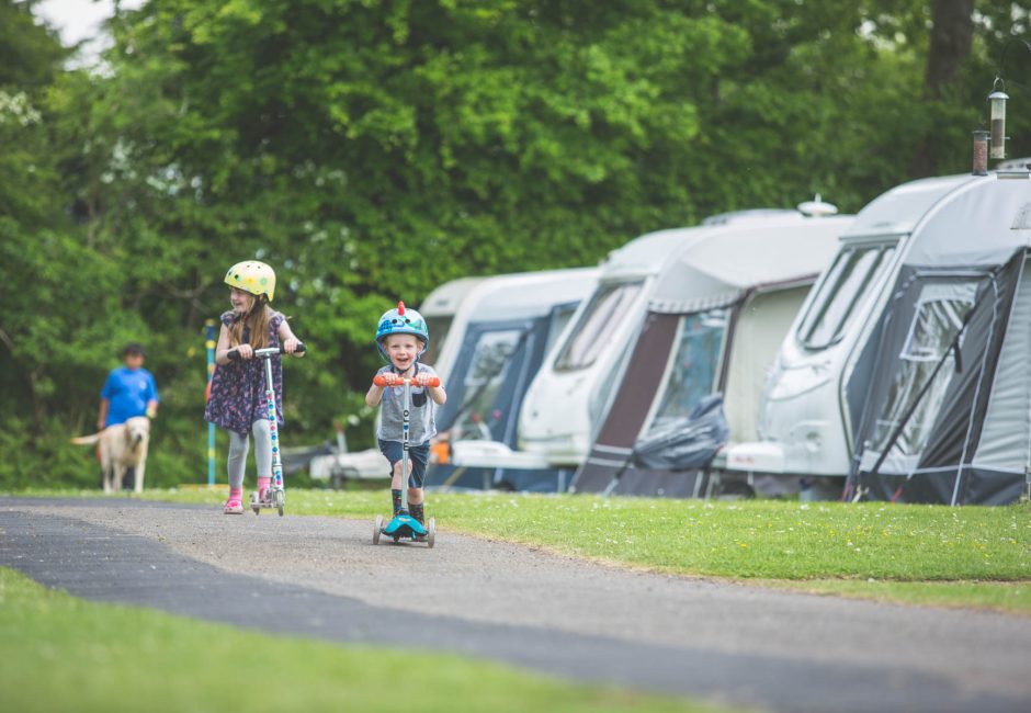 children playing on scooter by caravans at Forest Glade